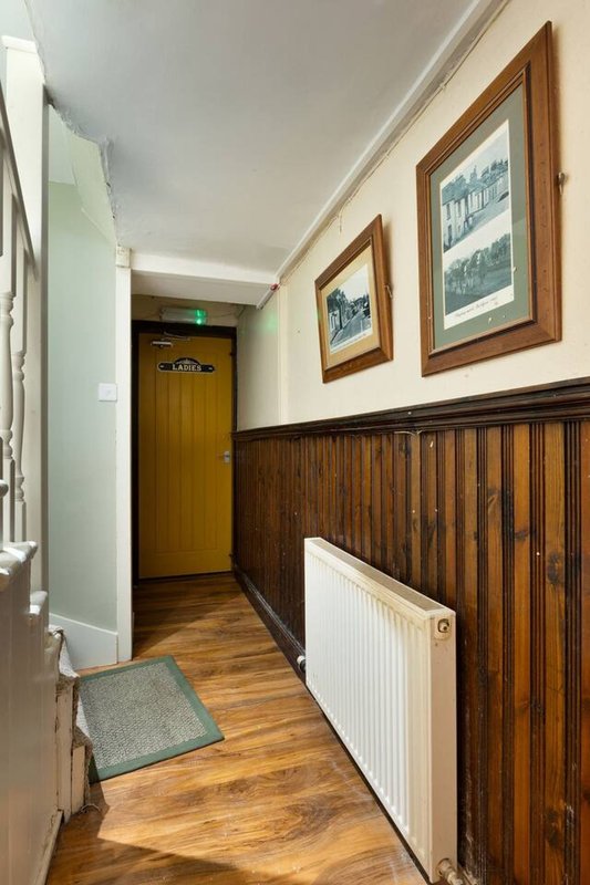 Hallway with wooden paneling, framed artwork on walls, radiator and wooden door