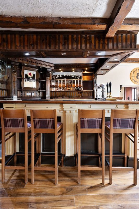 Rustic bar area with wooden beams, bar stools, and shelved spirits display