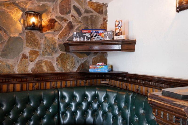 Stone fireplace with green leather tufted seating, wooden shelf with decorative items and lamp