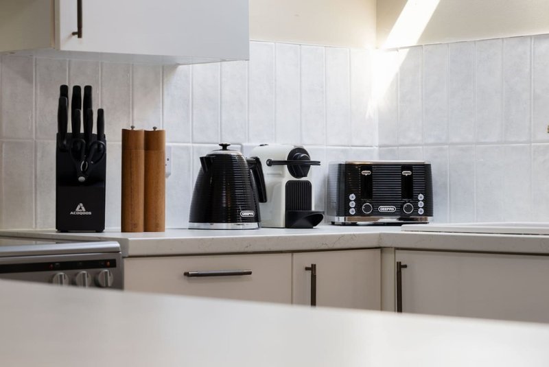 Modern kitchen countertop with appliances, knife block, and kitchen utensils on white tiled backsplash