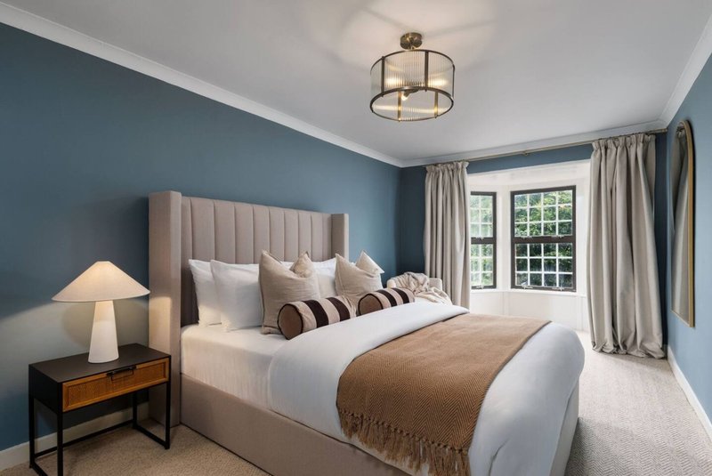 Modern bedroom with upholstered bed, teal walls, wooden nightstand and French doors