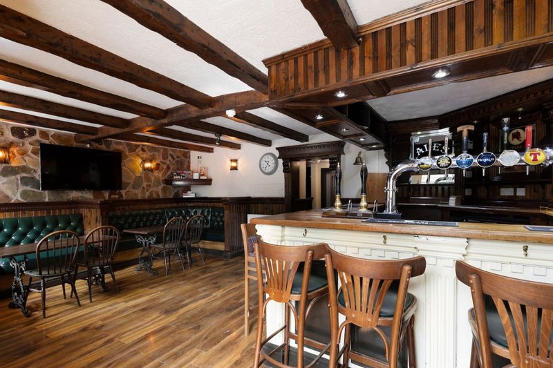 Large pub interior with wooden beams, bar counter, seating area and TV screen