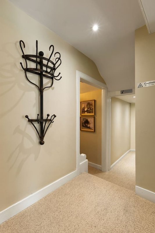 Hallway with beige carpet, cream walls, black coat rack, and doorways to adjacent rooms