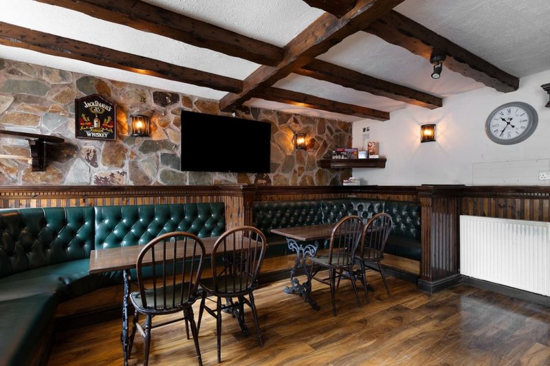 Rustic bar lounge with exposed beams, tufted seating, wooden chairs, stone fireplace and wall sconces