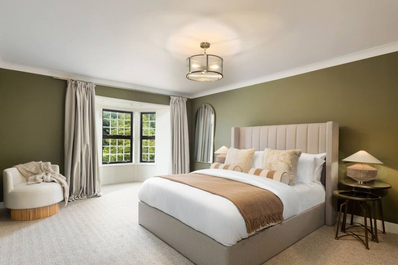 Spacious bedroom with double bed, cream headboard, olive walls, window seat and bedside lamp