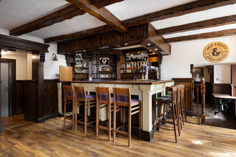 Home bar with wooden beams, bar stools, shelving with bottles, and hardwood flooring