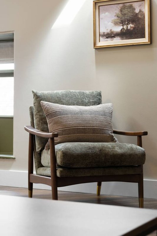 Mid-century modern wooden armchair with green upholstery and striped cushion near window