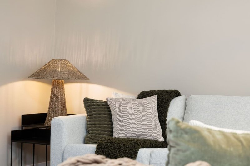 Modern living room with grey sofa, decorative cushions, and woven table lamp