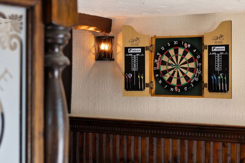 Recreation room wall with mounted dartboard, wooden cabinets, and wall sconce lighting