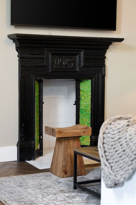 Modern living room with flat-screen TV, black ornamental fireplace, wooden stool and gray upholstered furniture