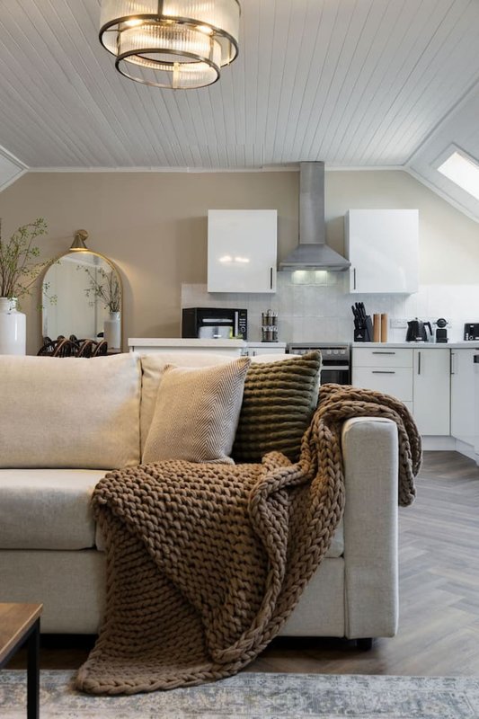 Open-plan living space with cream sofa, knit throw blanket, and modern kitchen with white cabinetry