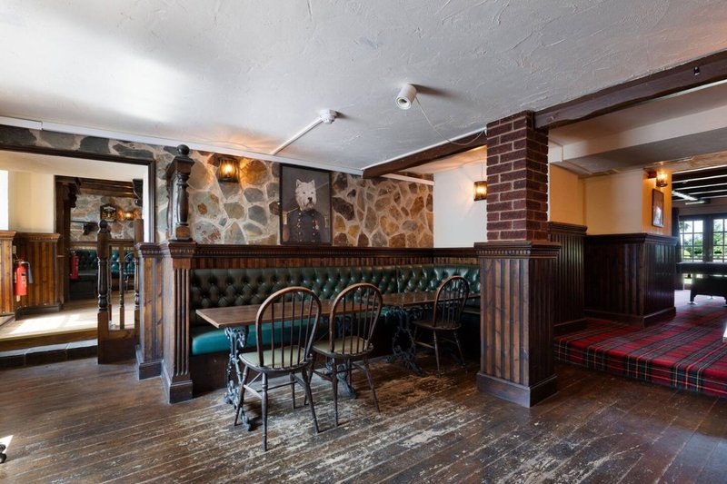 Open-plan bar and seating area with stone fireplace, wooden beams, chairs and dark furnishings