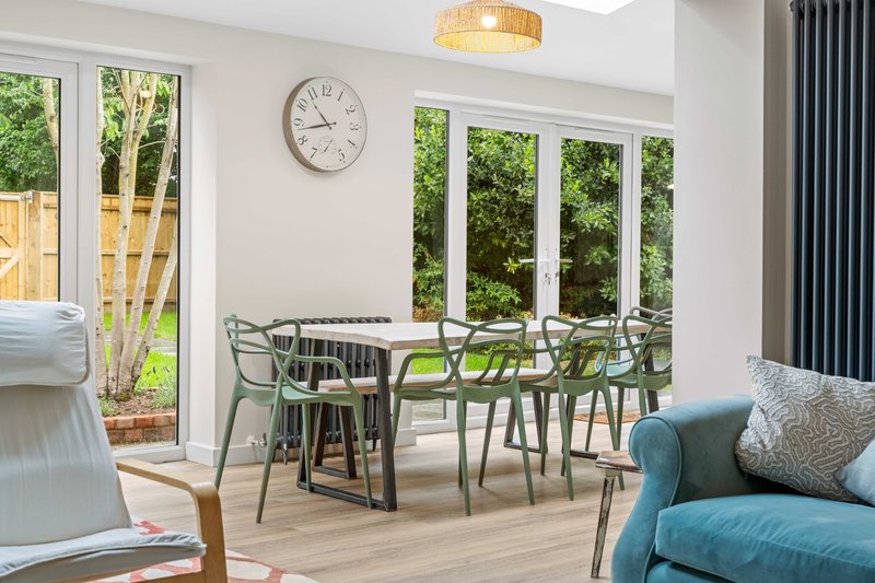 Bright dining area with green chairs, wooden table, and large windows overlooking garden