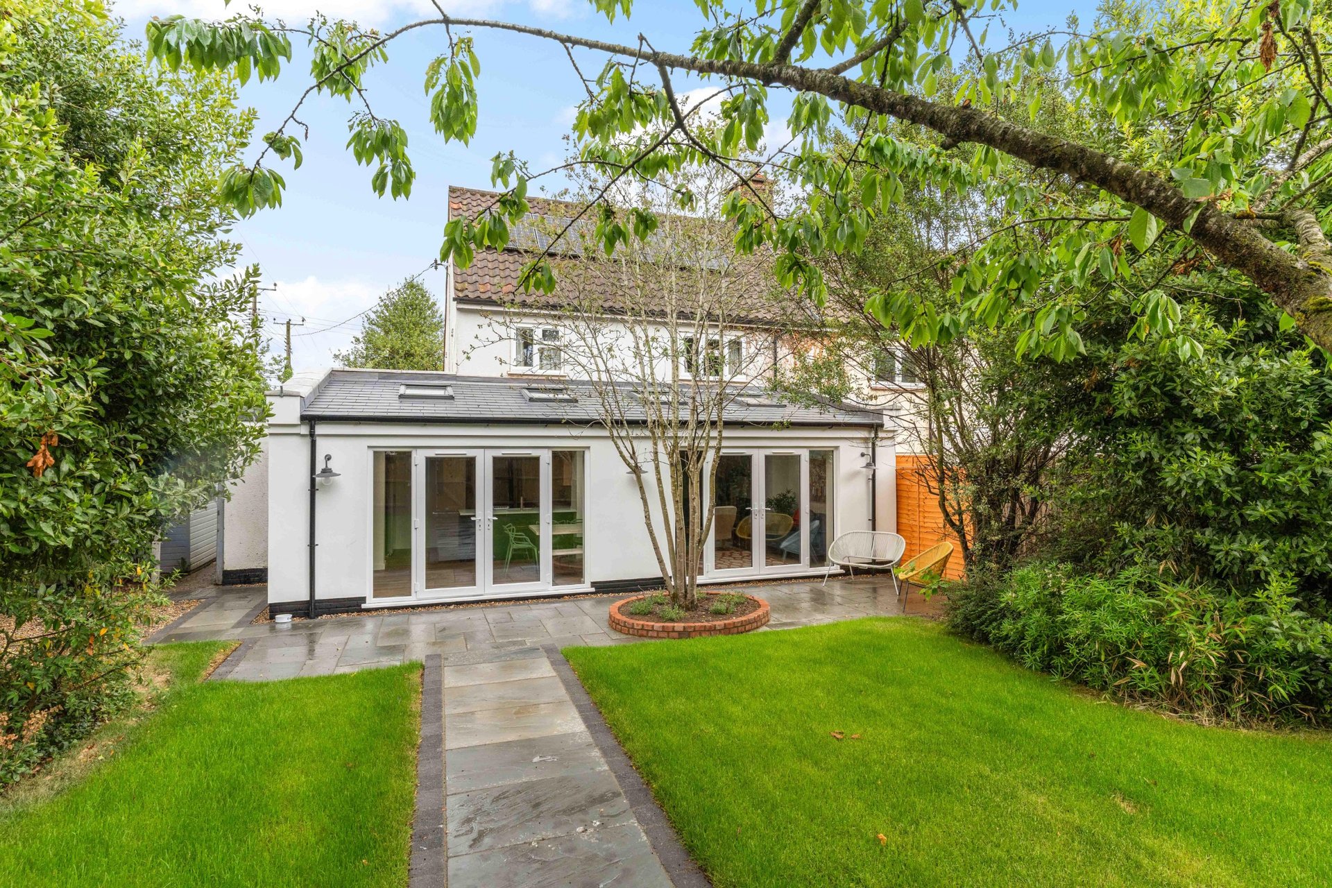 Modern white extension with large glass doors, manicured garden lawn and mature trees
