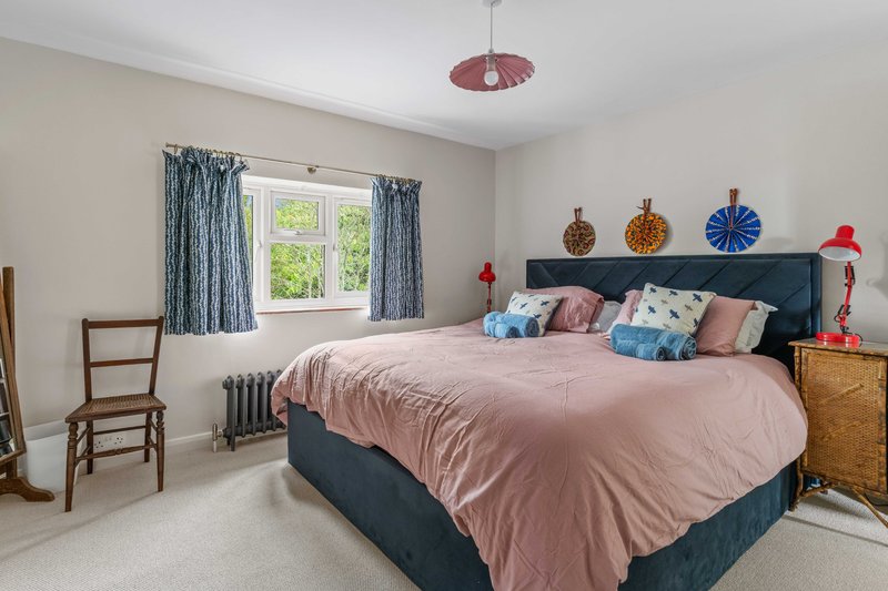 Spacious bedroom with double bed, patterned cushions, wooden chair, and colorful wall décor.