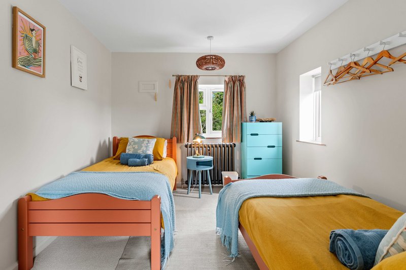 Bright children's bedroom with two single beds, colorful bedding, storage boxes and window with curtains.