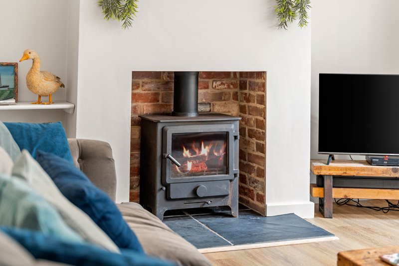 Living room with wood-burning stove, blue cushions, TV, and decorative accessories