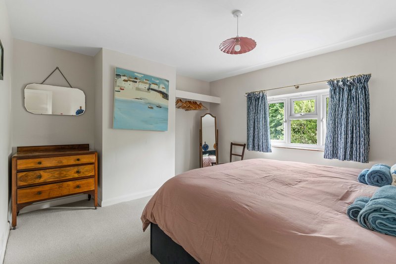 Bright bedroom with double bed, wooden dresser, framed artwork and blue curtains