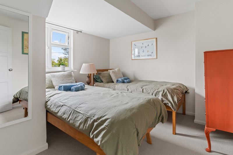 Bright bedroom with wooden bed, neutral bedding, window seat, and orange storage unit