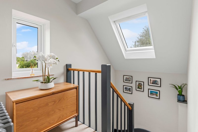 Bright attic bedroom with wooden chest, crib, framed photos, and skylight windows