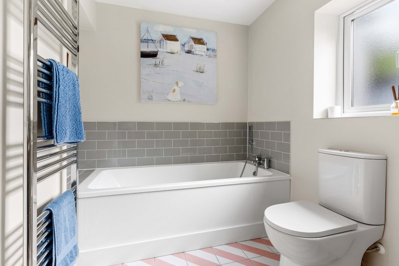 Modern bathroom with white bathtub, gray tile wall, toilet, towel rack and window