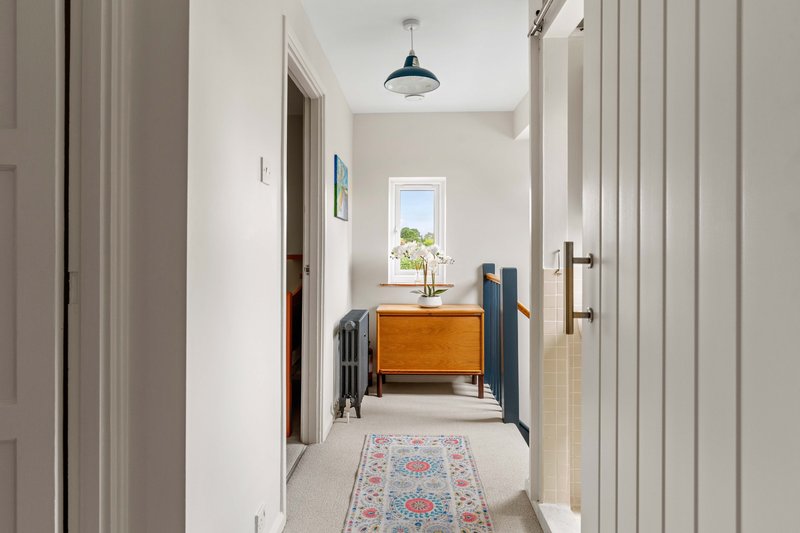 Bright hallway with wooden dresser, patterned runner rug, pendant light and window