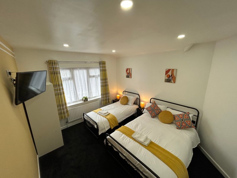 Twin bedroom with two single beds, wall-mounted TV, windows with checked curtains, and bedside lamps