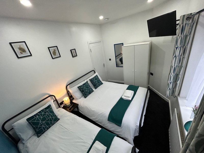 Twin bedroom with two single beds, white bedding, green accents, framed wall art and ceiling lights