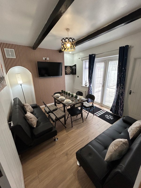Modern living room with black sofas, dining table, wall-mounted TV, and patio doors