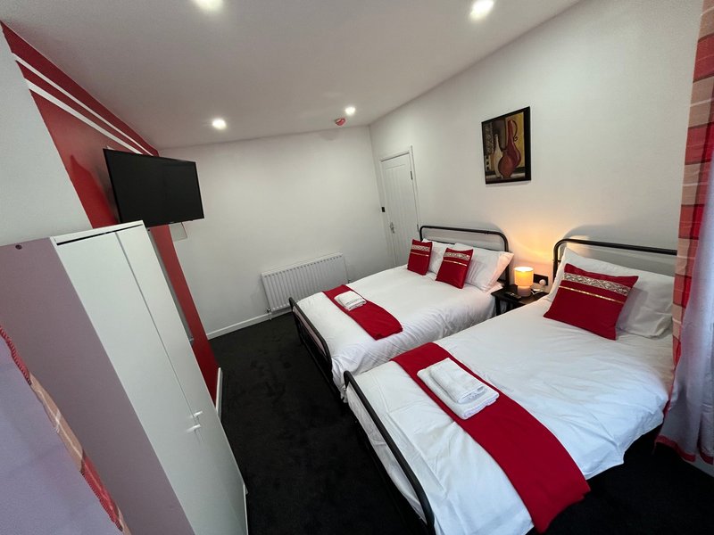 Twin bedroom with two single beds, red and white bedding, wall-mounted TV, and modern décor