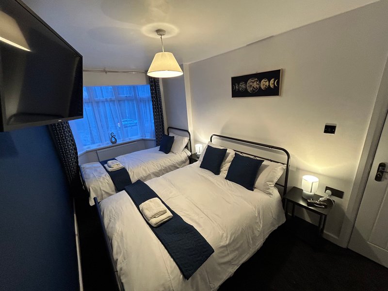 Modern bedroom with two single beds, pendant light, TV, and blue curtained window