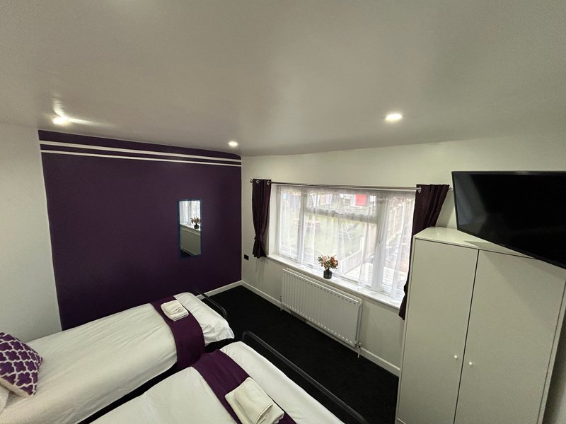 Modern bedroom with purple accent wall, double bed, window with curtains, TV and wardrobes