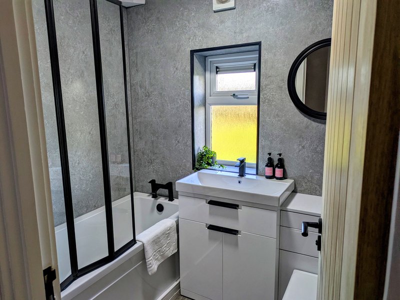 A modern, well-appointed bathroom with a full-size bath, overhead shower, contemporary vanity unit and WC, finished in a stylish grey and white design.