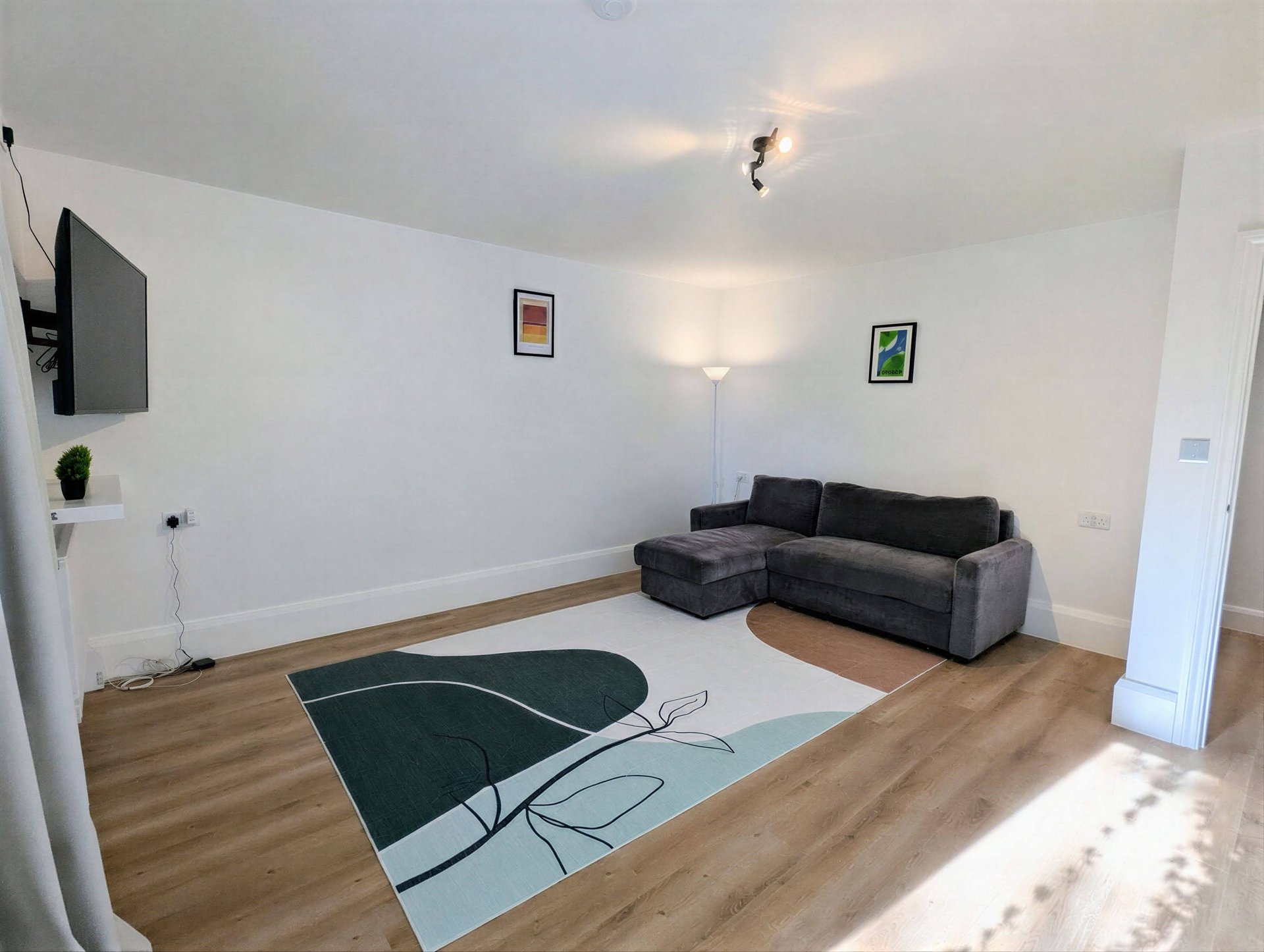 Modern living room with dark grey sofa, wooden floor, geometric area rug and wall-mounted TV