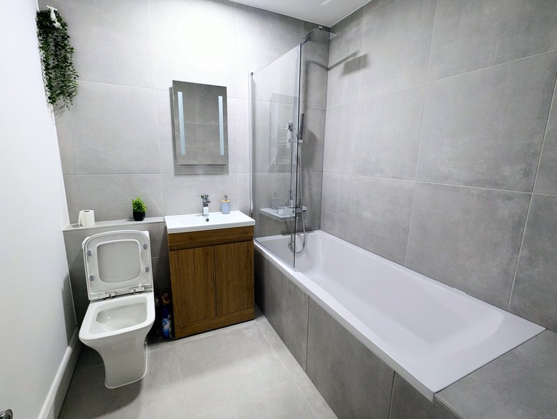 Modern bathroom with toilet, wooden vanity, sink, bathtub and glass shower enclosure
