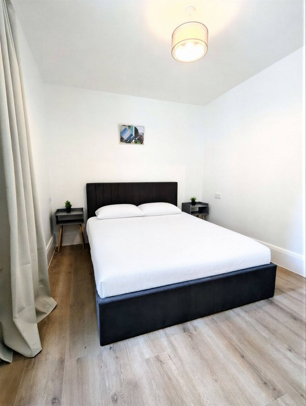 Modern bedroom with black bed frame, white bedding, wooden floor and ceiling light