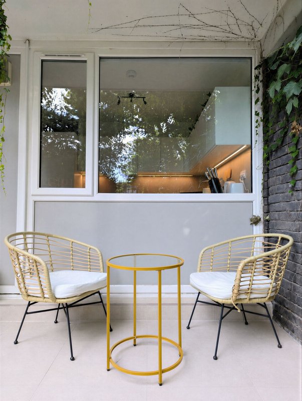 Patio seating area with two wicker chairs, yellow table, and large windows overlooking garden