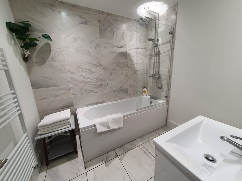 Modern bathroom with marble tiles, bathtub with glass screen, white sink and heated towel rail