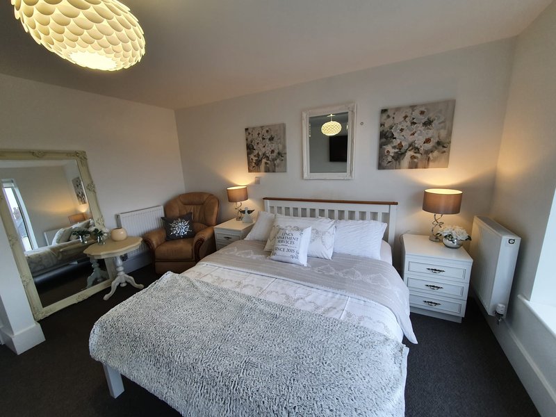 Bedroom with double bed, white headboard, bedside tables, desk, chair and wall art
