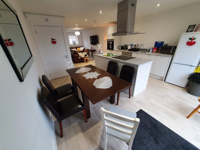 Open-plan kitchen and dining area with wooden table, black chairs, white cabinetry and stainless steel appliances