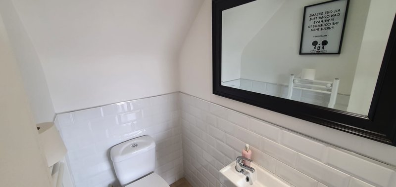 Small bathroom with white subway tile walls, toilet, sink and framed wall art