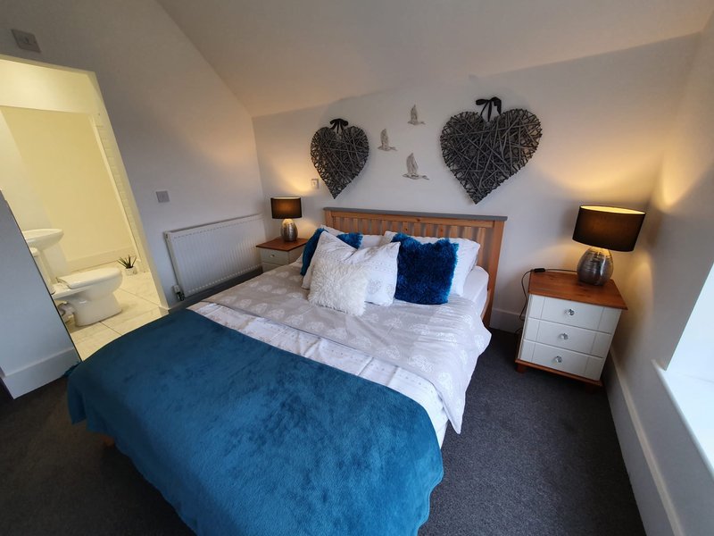 Modern bedroom with double bed, blue throw, wooden headboard, bedside tables and wall decor