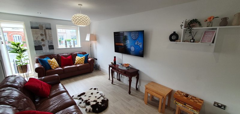 Modern living room with brown leather sofa, wall-mounted TV, wooden furniture and decorative shelving
