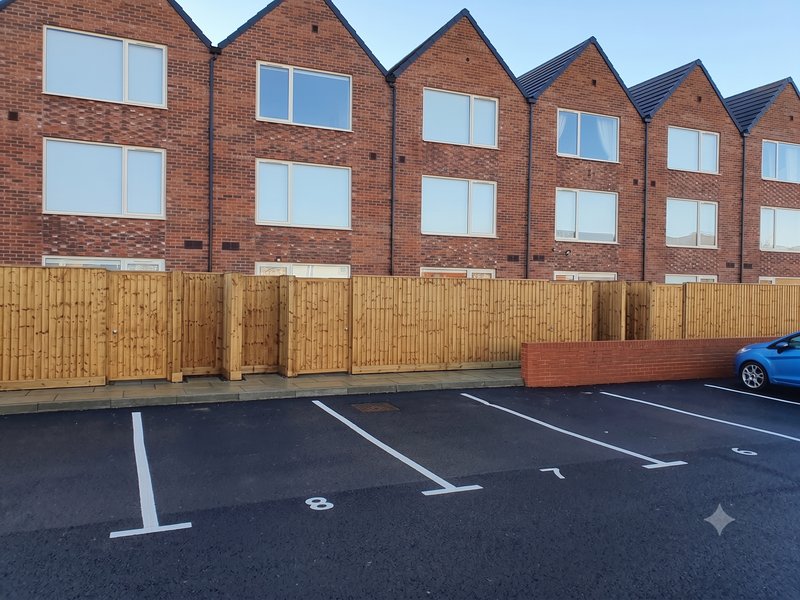 Modern brick townhouse building with wooden fence and allocated parking spaces
