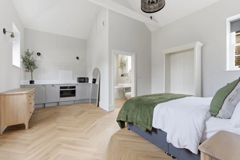 Studio bedroom with double bed, kitchenette, wooden flooring and bright windows