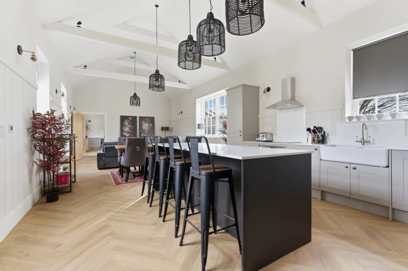 Open-plan kitchen and dining area with black island, bar seating, pendant lights, and wooden flooring