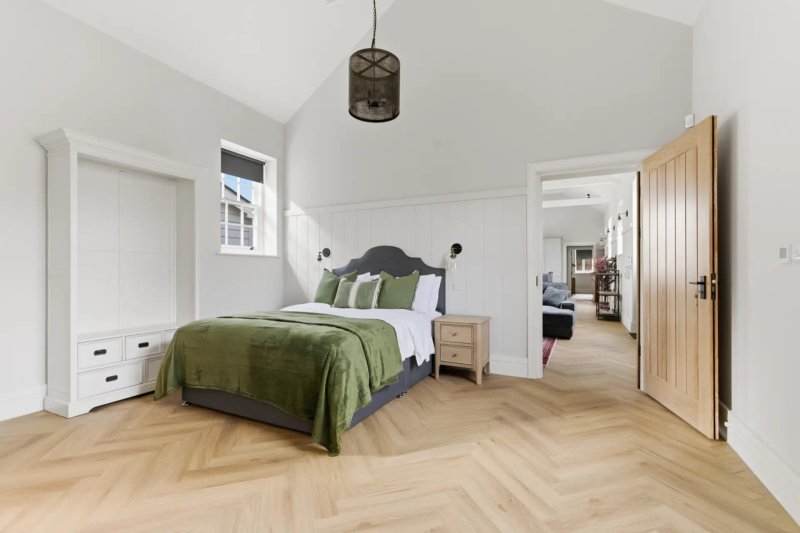 Spacious bedroom with double bed, green bedding, wooden flooring, white walls and pendant light