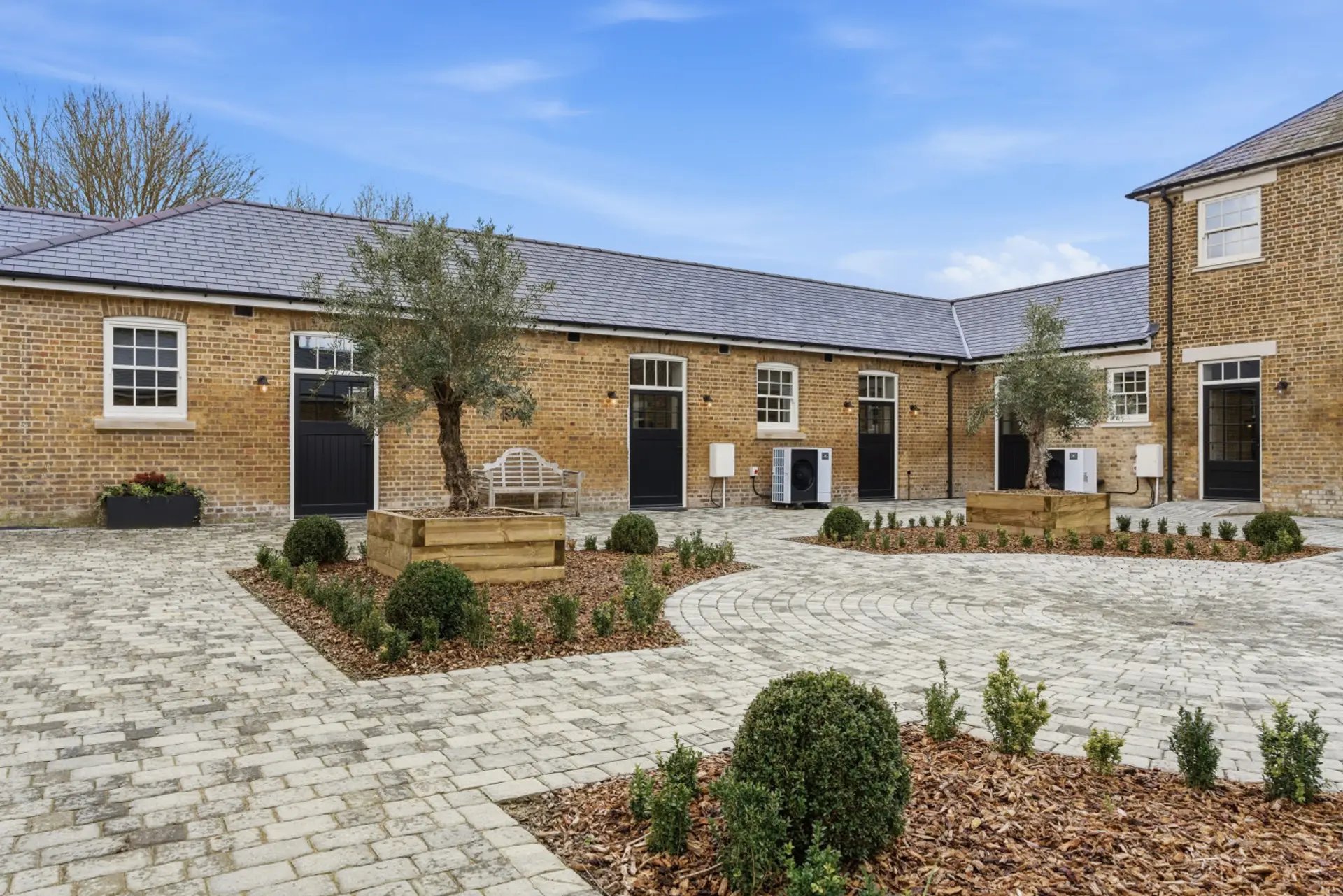 Modern brick courtyard property with paved entrance, manicured landscaping and multiple doors