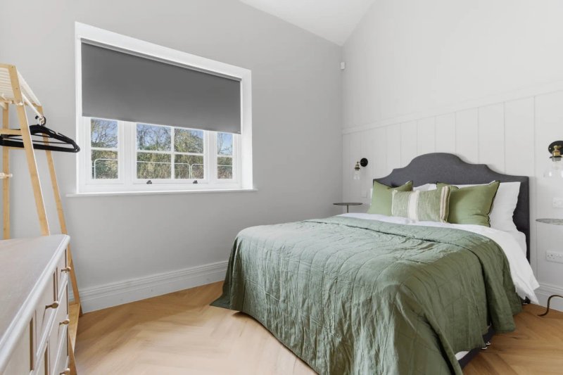 Bright bedroom with double bed, green bedding, wooden floor and large window