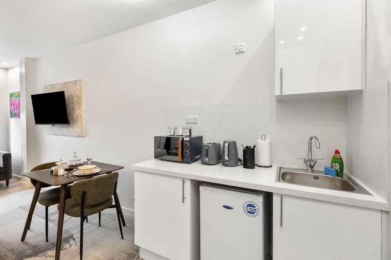Modern kitchen with white cabinetry, sink, and countertop appliances, adjacent dining area with wooden table